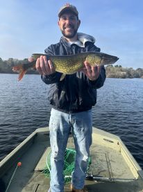 Angler proudly displaying a Northern Pike while fishing from a small boat on a serene lake.