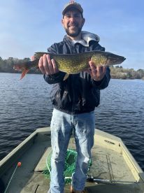 Angler proudly displaying a Northern Pike while fishing from a small boat on a calm lake.