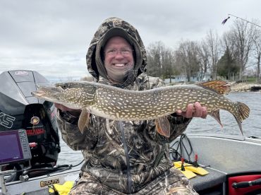 An angler proudly displaying a large Northern Pike while fishing from a boat, showcasing the excitement of a successful catch.
