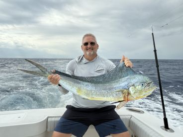 An angler proudly displaying a large Mahi Mahi while aboard a fishing boat in open waters.