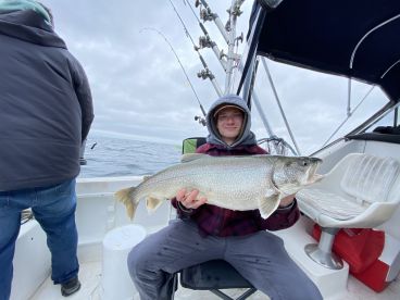A young angler proudly displaying a large Lake Trout while fishing on a boat in open waters.