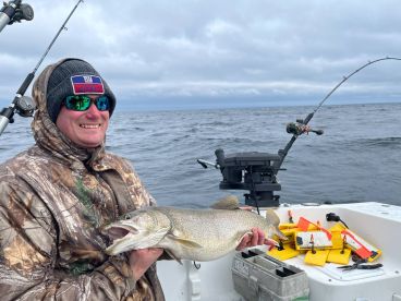 Angler displaying a large Lake Trout while fishing on a boat in open waters, showcasing the thrill of the catch.