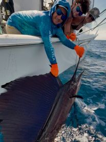 A young angler and friends proudly displaying a large Sailfish while fishing offshore, showcasing the excitement of deep-sea fishing.