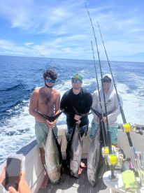 Three anglers proudly displaying their large Yellowfin Tuna while on a sportfishing boat in open waters.