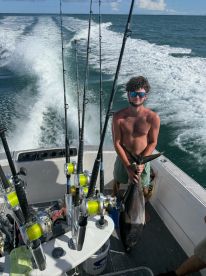 A young angler proudly displaying a large tuna while aboard a fishing boat, with the ocean waves in the background.