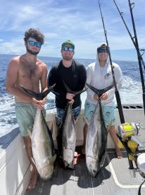 Three anglers proudly displaying their catch of large Yellowfin Tuna while on a sportfishing trip in open waters.
