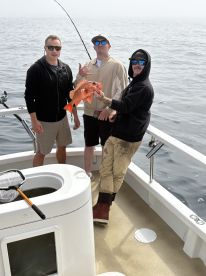 Three anglers proudly displaying a vibrant Red Snapper aboard a fishing boat, showcasing a successful day on the water.