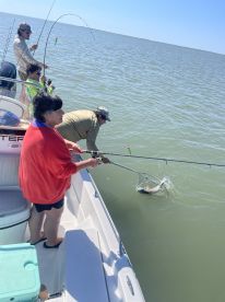 A family fishing trip in progress, with an angler using a net to catch a fish while others assist from the boat.