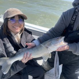 A smiling angler proudly displays a large Walleye while fishing on a boat, showcasing a successful day on the water.