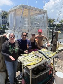 A group of four anglers proudly displaying their catch of Mahi Mahi on a dock after a successful fishing trip.