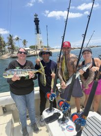 A group of four anglers proudly displaying their catch of Mahi Mahi while fishing near a lighthouse, showcasing a vibrant day on the water.