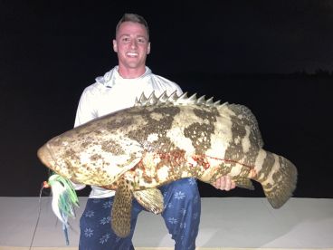 An angler proudly displaying a large Goliath Grouper caught during a nighttime fishing trip.