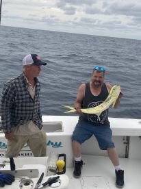 Two anglers aboard a fishing boat, with one proudly displaying a vibrant Mahi Mahi caught during a deep-sea fishing trip.