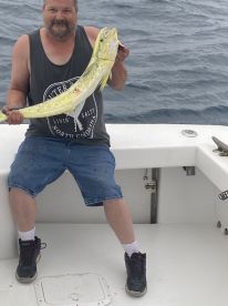 An angler proudly displaying a large Mahi Mahi aboard a fishing boat, showcasing a successful offshore fishing trip.