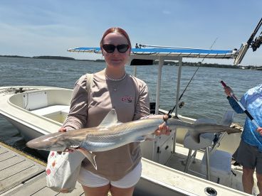 An angler proudly displaying a caught shark while standing on the dock next to a fishing boat, showcasing a successful day on the water.