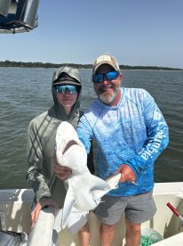 A young angler and an adult proudly displaying a caught shark while fishing on a boat, showcasing a successful day on the water.