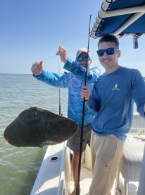A young angler and an adult proudly display a large stingray caught during a fishing trip, showcasing the excitement of fishing in coastal waters.