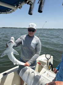A young angler proudly displaying a caught shark while aboard a fishing boat in a coastal waterway.