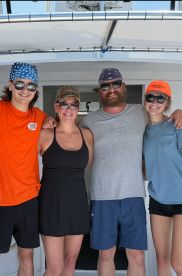 A group of four individuals posing together on a fishing charter boat, showcasing a fun day out on the water.