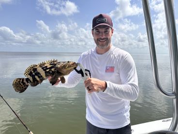 Angler holding a large Goliath Grouper while fishing on a boat in calm waters, showcasing a successful catch.