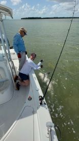 Two anglers on a boat engaging in a fishing activity, with a shark visible in the water, showcasing an exciting moment on a coastal fishing trip.
