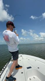 Angler reeling in a catch while fishing on a boat in calm waters, showcasing an exciting moment during the trip.