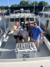 A group of anglers proudly posing on a fishing charter boat with a catch of striped bass displayed on a cooler.