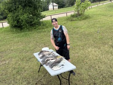 Angler proudly displaying a variety of catfish on a table after a successful fishing trip.