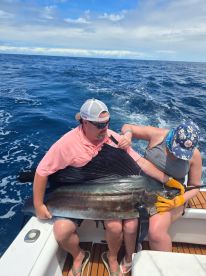 Two anglers working together to reel in a large Sailfish while on a deep-sea fishing trip.