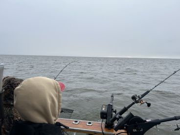 A young angler is actively fishing from a boat, with a bent rod indicating a catch in progress on a cloudy day.