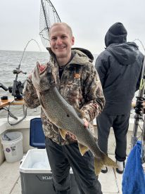 Angler proudly displaying a large Lake Trout while fishing on a boat in overcast conditions.