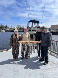 A group of anglers proudly displaying their catch of multiple fish on a dock, with a boat in the background, after a successful fishing trip.