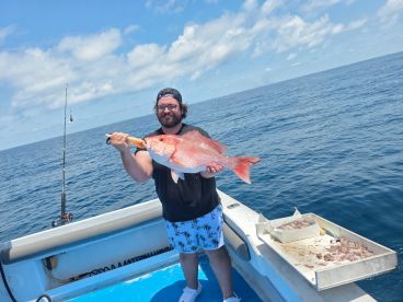 An angler proudly displaying a large Red Snapper while fishing offshore, showcasing a successful day on the water.