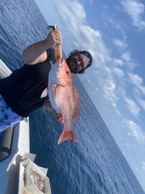 An angler proudly displaying a large Red Snapper while fishing offshore, showcasing a successful day on the water.
