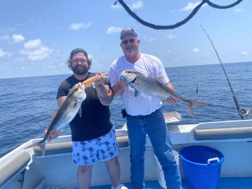 Two anglers proudly displaying their catches, a large fish each, while fishing offshore in clear blue waters.