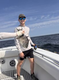 A young angler proudly displaying a caught fish while aboard a boat, enjoying a day of fishing on open waters.
