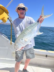 An angler proudly displaying a large Jack Crevalle while fishing on a boat in clear blue waters.