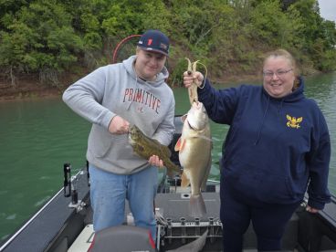 Two anglers proudly displaying their catch, including a large Largemouth Bass and a sizable Walleye, while fishing from a boat on a serene lake.