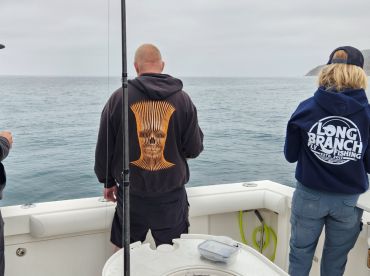 Three anglers are engaged in fishing on a boat, with a calm ocean backdrop, showcasing a relaxed fishing environment.