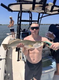Angler proudly displaying a large Speckled Trout while fishing on a boat in a coastal waterway.