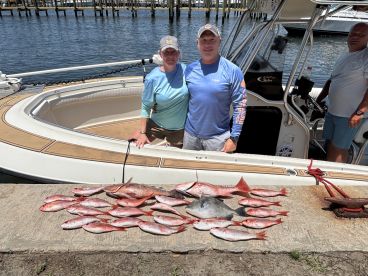 A group of anglers proudly displaying their catch of Red Snapper and other species on a dock beside their boat after a successful fishing trip.
