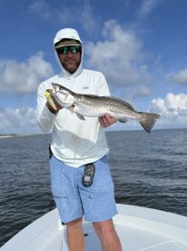 Angler displaying a large Speckled Trout while fishing on a boat in a coastal waterway.