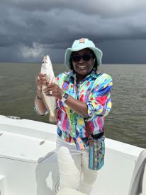 Angler proudly displaying a Speckled Trout while fishing on a boat, with stormy skies in the background.