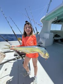 A young angler proudly displaying a vibrant Mahi-Mahi aboard a fishing boat, showcasing a successful day on the water.