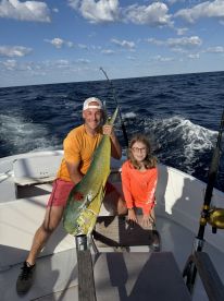 A young girl and an adult proudly display a large Mahi Mahi on a fishing boat, enjoying a day out on the open water.