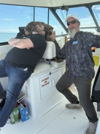 Two anglers relaxing inside the cabin of a fishing boat, one posing playfully while the other rests.