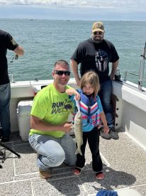 A young girl proudly displaying her catch, a fish, alongside her father on a fishing boat, enjoying a family outing.