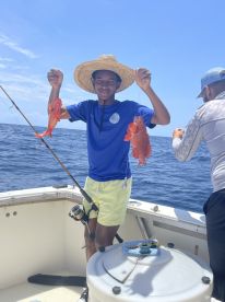 A young angler proudly displaying two vibrant Red Snapper while fishing offshore, showcasing a successful day on the water.