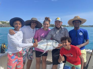 A group of young anglers proudly displaying a large Trevally on a fishing charter in clear blue waters.