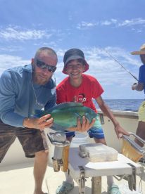 A young angler and an adult proudly displaying a vibrant Blue Parrotfish aboard a fishing boat, enjoying a sunny day on the water.
